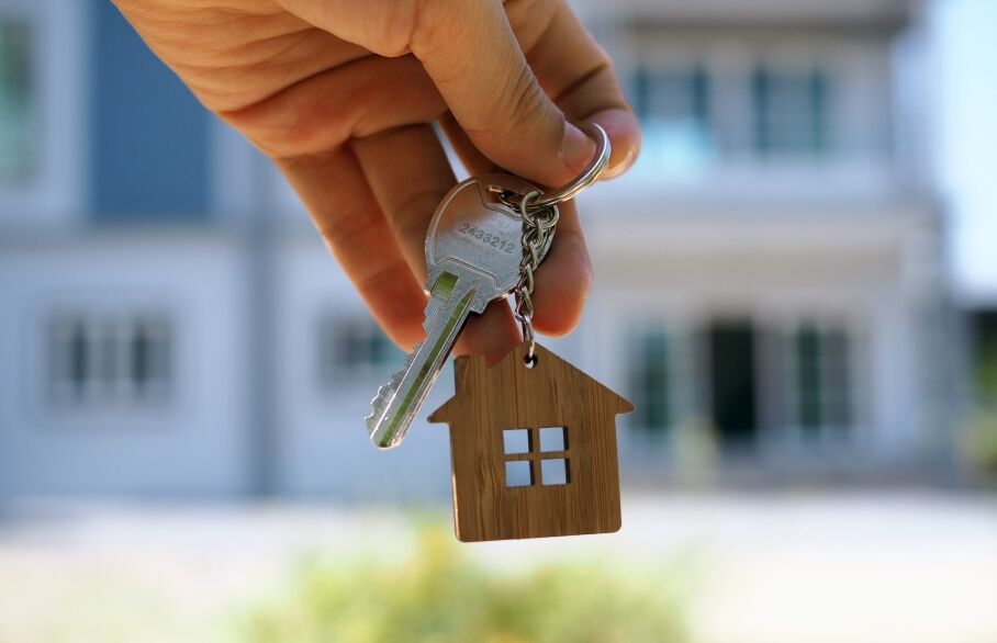 A hand holding a key in front of a house