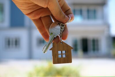 A hand holding a key in front of a house